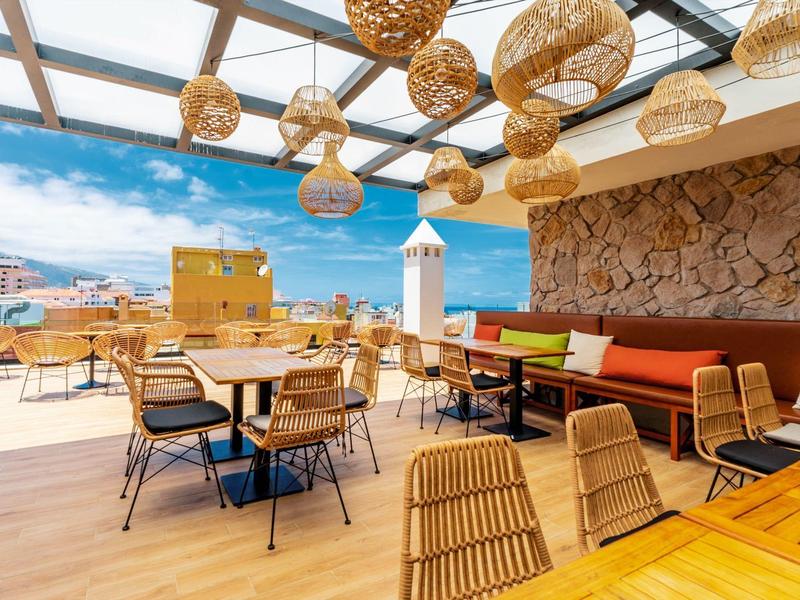 Terrasse extérieure lumineuse avec meubles en rotin et vue sur la mer sous un toit en verre.