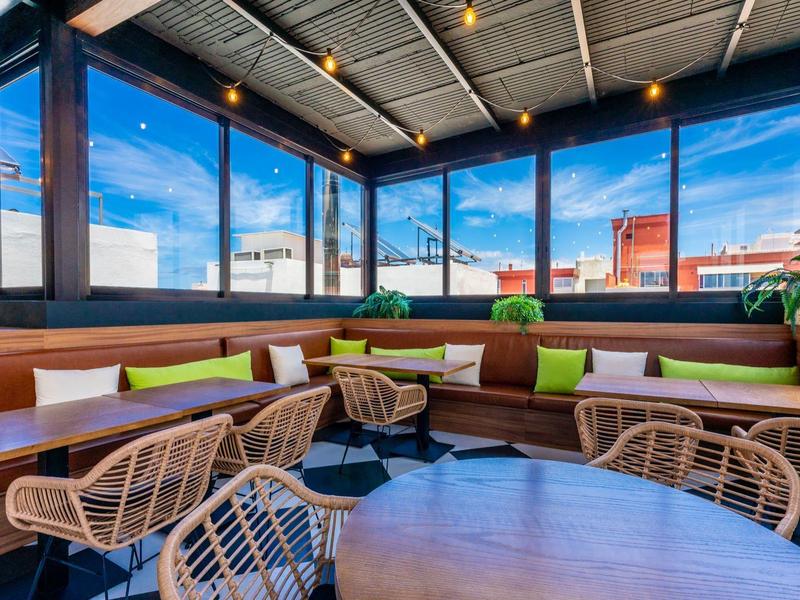 Terrasse sur le toit moderne avec coin salon, chaises en osier et fenêtres panoramiques en plein jour.