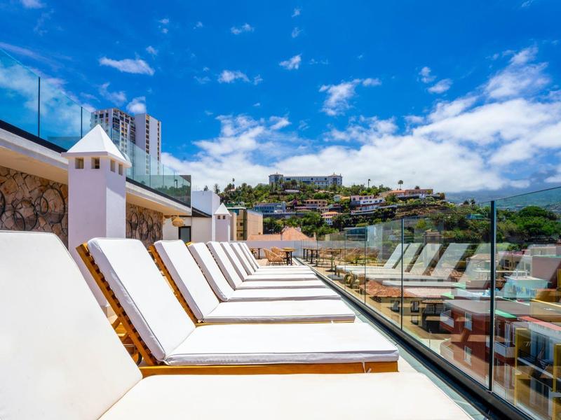 Rangée de chaises longues blanches sur une terrasse avec vue sur une ville et un ciel bleu.
