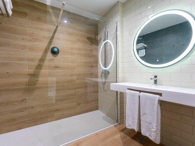 Salle de bain moderne avec miroir ovale éclairé, lavabo et douche à l'italienne avec mur effet bois.