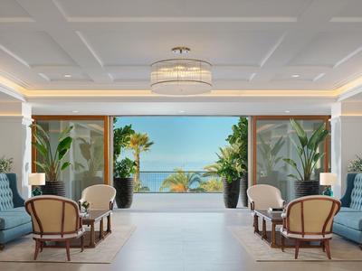 Elegante hall dell'hotel con aree salotto e vista su palme e mare.