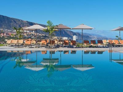 Infinity-Pool mit Liegestühlen und Schirmen vor Bergkulisse und klarem Himmel