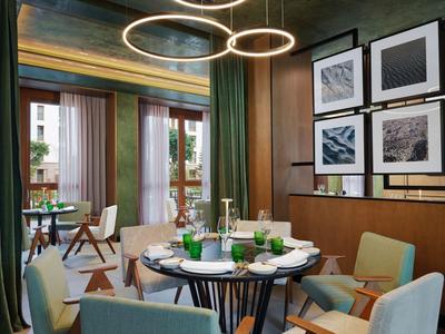 Modern hotelrestaurant met ronde tafels, groene stoelen en grote ramen met uitzicht op de stad.