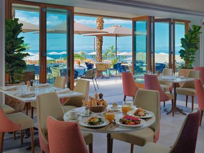 Modern restaurant met uitzicht op zee, gedekte tafels en comfortabele stoelen binnen en buiten.
