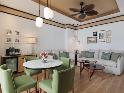 Helles Wohnzimmer mit grünen Sesseln, rundem Esstisch und zwei Sofas in einem Hotelzimmer.