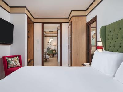 Modern eingerichtetes Hotelzimmer mit großem Bett, grünem Kopfteil und rotem Sessel.