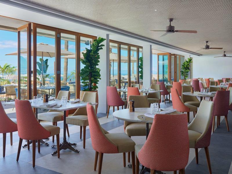 Ristorante luminoso con sedie rosa, grandi finestre e vista sul mare.