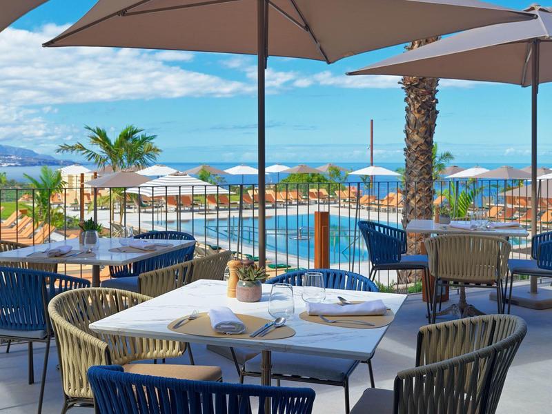 Area terrazza con tavoli, sedie e grandi ombrelloni accanto a una piscina con vista mare.