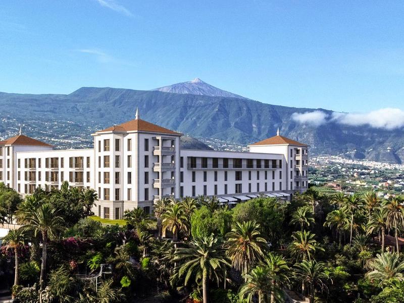 Hotel con edificio bianco e tetti rossi davanti a uno sfondo montano e palme