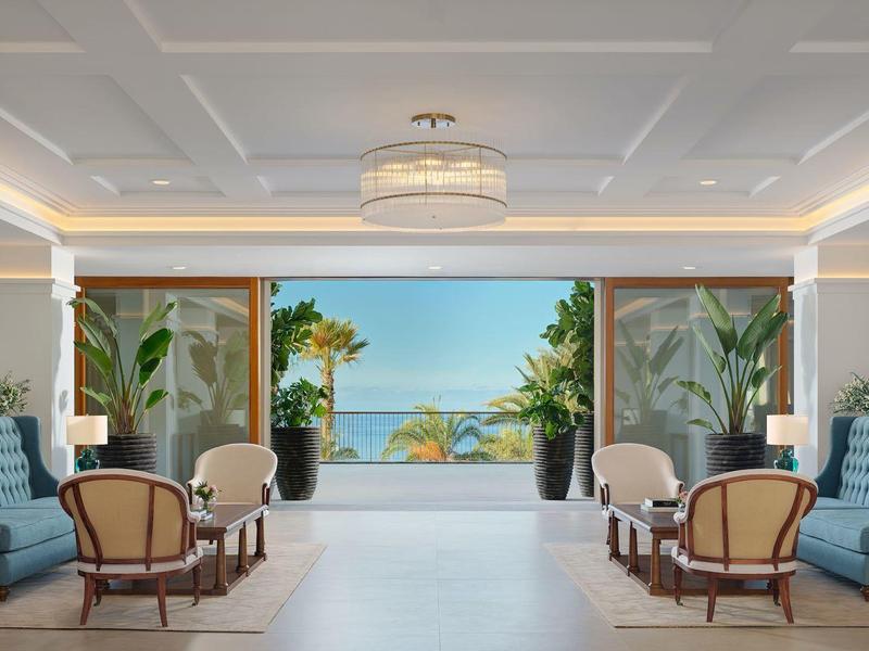 Elegante hall dell'hotel con aree salotto e vista su palme e mare.