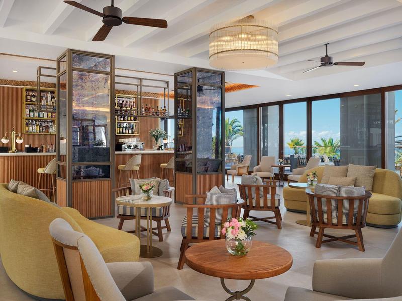 Lounge d'hotel luminosa con poltrone comode, tavoli e grandi finestre.