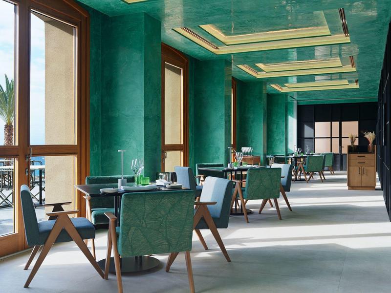 Elegante area lounge dell'hotel con pareti verdi e sedute accanto a grandi finestre.