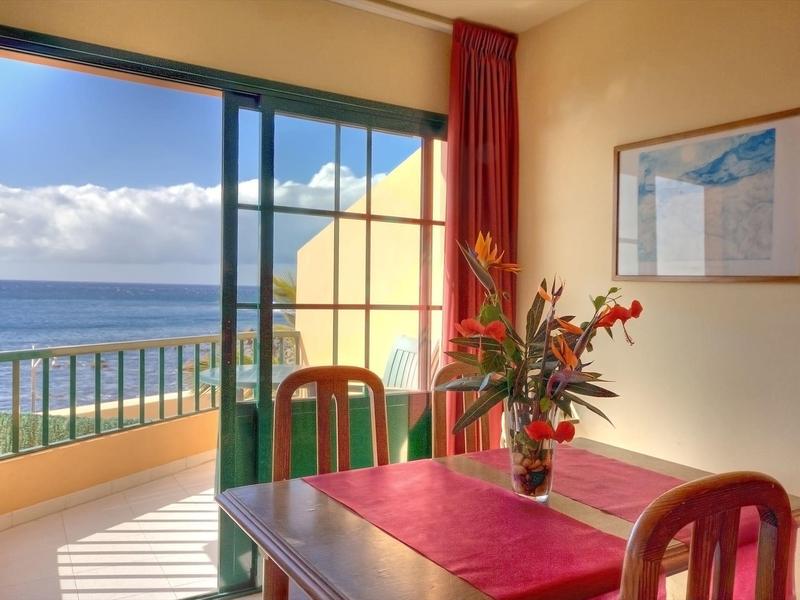 Jídelní kout s výhledem na moře a terasu přes otevřené posuvné skleněné dveře.