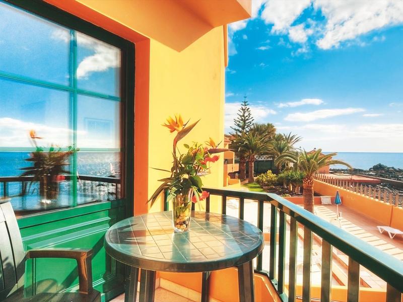 Terasa s kulatým skleněným stolem, židlemi a výhledem na moře za jasné oblohy