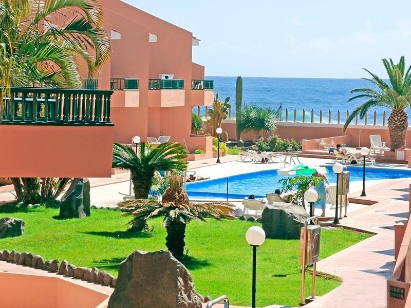 Hotelový komplex s bazénem, palmami a výhledem na moře za slunečného dne