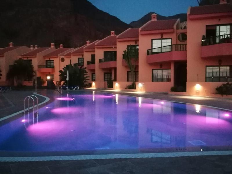 Osvětlený bazén před hotelem s horami v pozadí při soumraku.