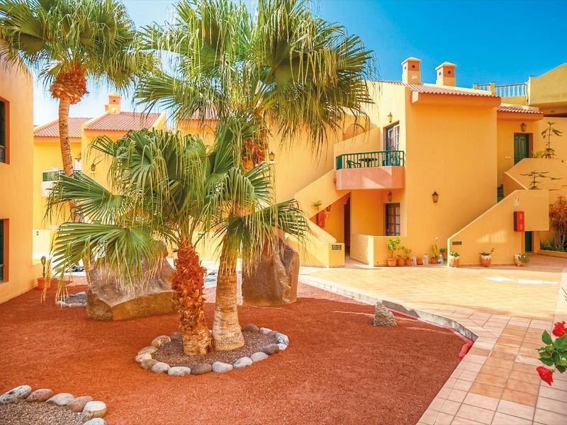 Nádvoří hotelu s palmami a žlutými budovami pod modrou oblohou.