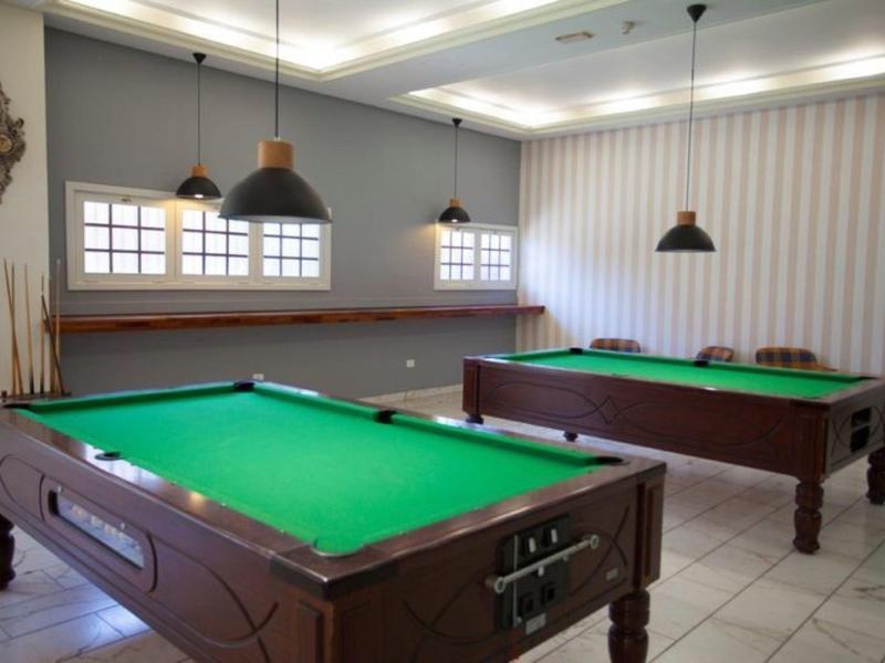 Stanza con due tavoli da biliardo in legno, panno verde, lampade a sospensione e finestre con tende.