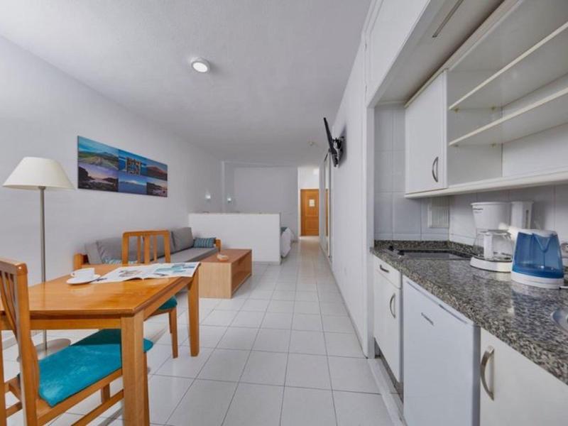 Monolocale moderno con cucina e tavolo da pranzo, letto sullo sfondo, interno luminoso e pulito.