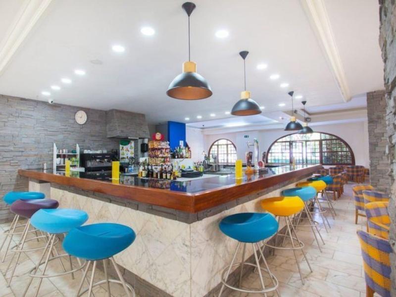 Bar moderno dell'hotel con sgabelli colorati e pareti in mattoni a vista sotto lampade a sospensione luminose.