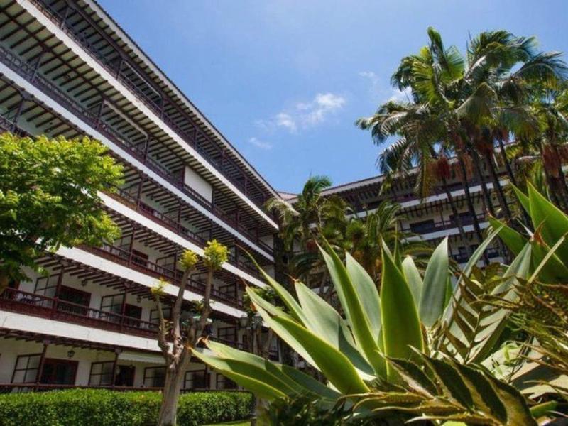 Cortile dell'hotel con balconi, piante verdi lussureggianti e cielo azzurro limpido.