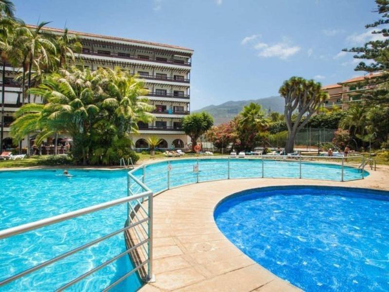 Resort con piscina esterna curva, acqua blu chiara e hotel multi-piano sullo sfondo.