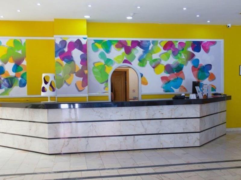 Reception dell'hotel con murales astratti colorati su pareti gialle dietro un bancone in marmo bianco.