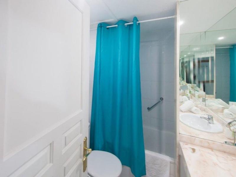 Piccolo bagno con tenda da doccia blu, pareti bianche e piano in marmo con lavabo.