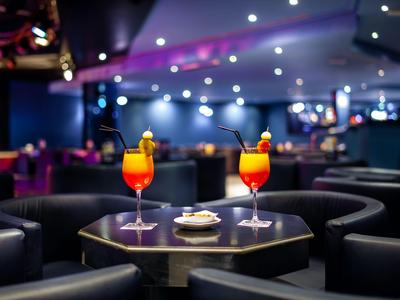 Zwei bunte Cocktails auf einem kleinen runden Tisch in einer stilvollen Hotelbar mit Sitzgelegenheiten.