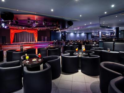 Spazio eventi moderno con palco, tende rosse e sedute nere in un'atmosfera elegante.