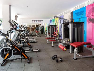 Fitnessraum mit Fahrradergometern, Gewichten und farbigen Wänden in modernem Design.