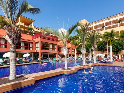 Grande piscina dell'hotel con palme e ombrelloni sotto un cielo azzurro.