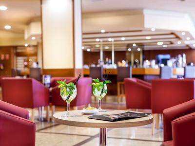 Lounge d'hotel moderna con poltrone rosse e bevande su un tavolo rotondo.