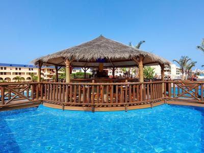 Blick auf einen Pavillon über einem Pool mit klarem blauem Wasser und Hotelgebäuden im Hintergrund.