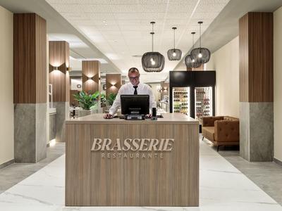 Elegante Hotelbar mit modernem Holztresen, Deckenleuchten und gemütlicher Sitzgruppe im Hintergrund.