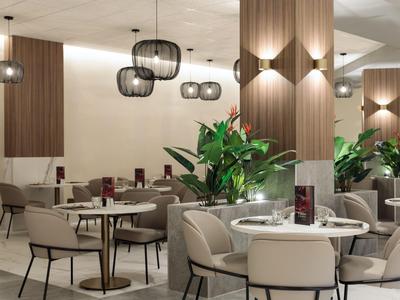 Moderner Hotelrestaurantbereich mit runden Tischen, bequemen Stühlen und grünen Pflanzen.