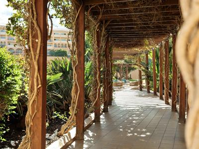 Sonnendurchfluteter Weg mit Holzsäulen und rankenden Pflanzen in einem Hotelgarten.