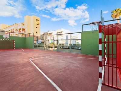 Outdoor-Sportplatz mit rotem Boden neben Hotels unter blauem Himmel.