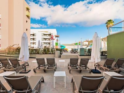 Hotelterrasse mit bequemen Liegestühlen und Sonnenschirmen unter blauem Himmel.