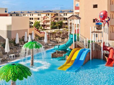 Bunter Wasserpark mit Rutschen und Spielgeräten in einem Hotelpool bei Sonnenschein.
