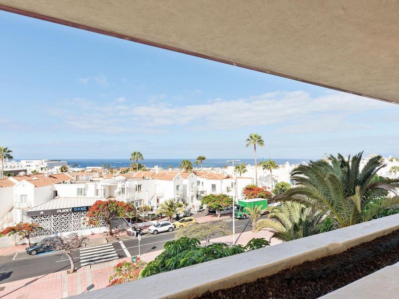 Vista dal balcone sulla città con case bianche, palme e mare all'orizzonte.