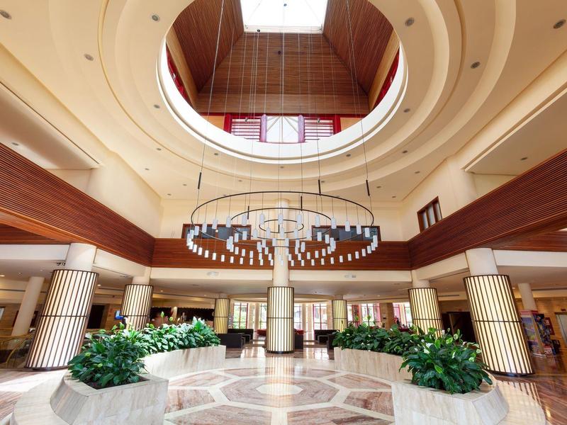 Ampia hall d'hotel elegante con atrio, colonne, piante e illuminazione moderna.