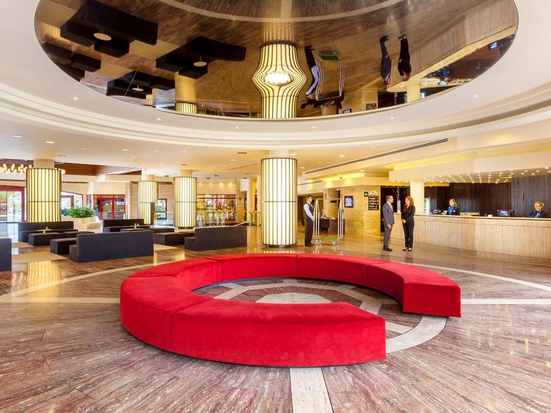 Moderna hall dell'hotel con panchina rotonda rossa e pavimento chiaro in marmo.