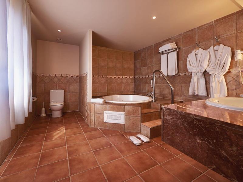 Ampio bagno d'hotel con vasca angolare, doccia, WC e accappatoi appesi al muro.