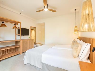 Chambre d'hôtel lumineuse avec deux lits, meubles en bois et ventilateur au plafond.