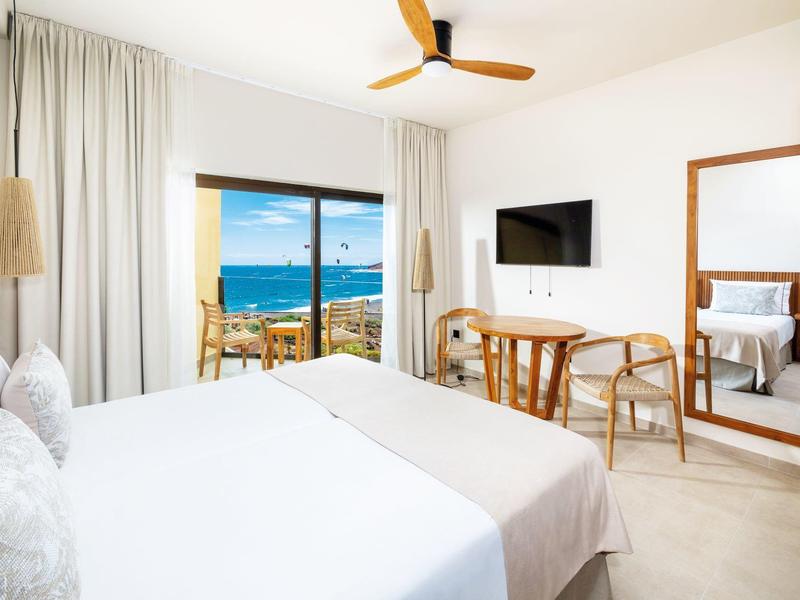 Chambre d'hôtel lumineuse avec lit double, bureau, grand miroir et vue sur la mer.