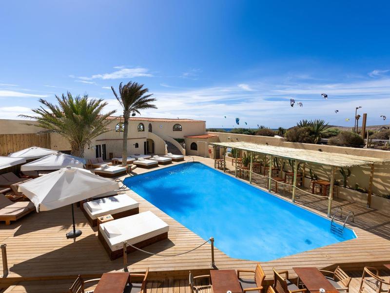 Piscine extérieure accueillante avec chaises longues et parasols devant un bâtiment clair sous un ciel bleu.