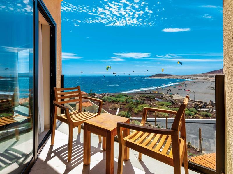 Balcon avec mobilier en bois et vue sur la mer sous un ciel ensoleillé sur la côte.