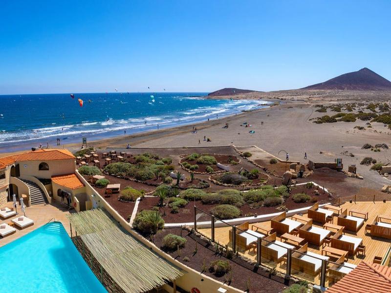 Hôtel en bord de mer avec piscine, chaises longues et vue sur la plage et la mer bleue.