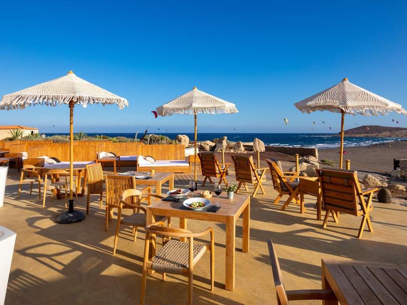 Terrasse avec meubles en bois et parasols au bord de la mer par une journée ensoleillée.